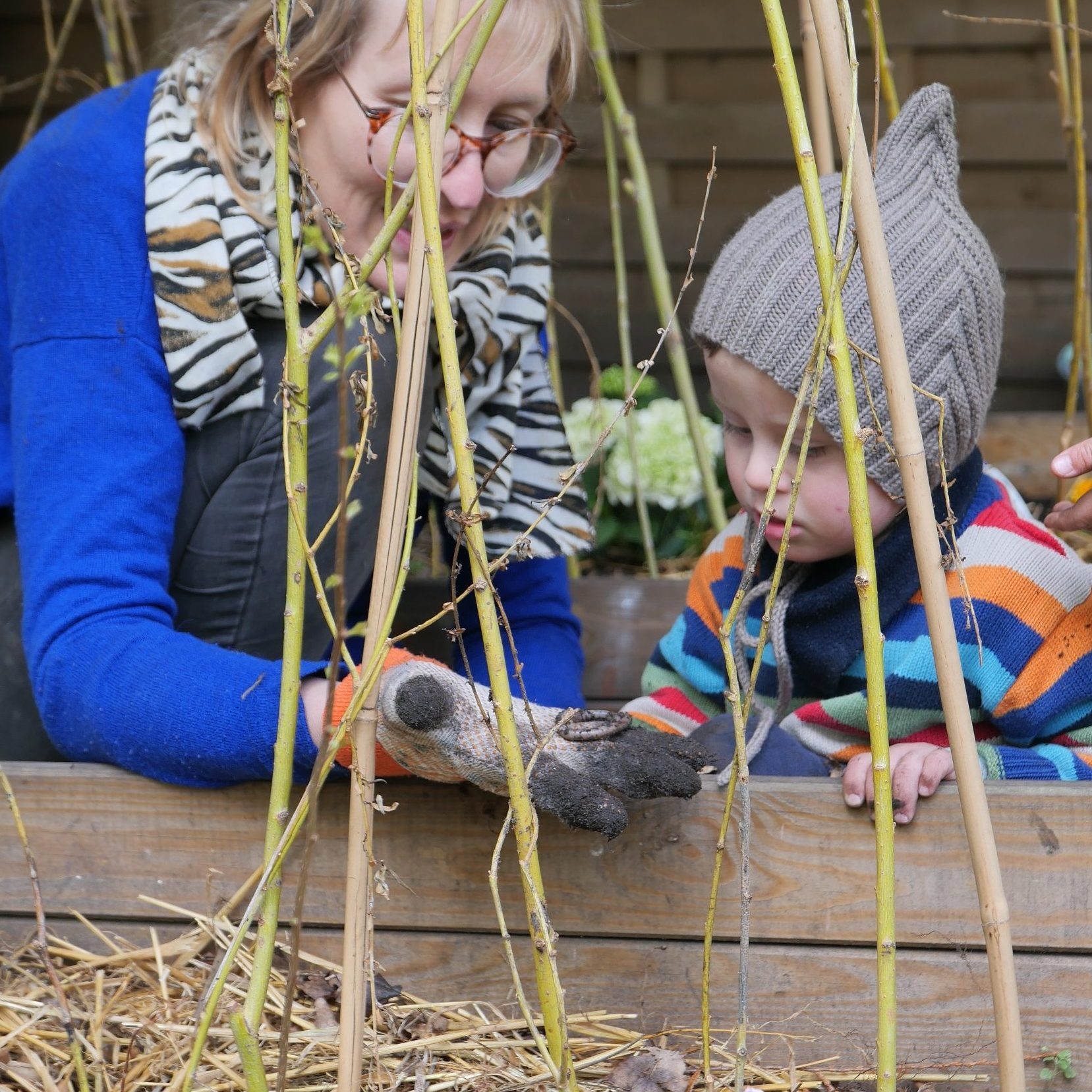 Anne-CHarlotte Viriot zeigt einen Kind mit Down Syndrom was sie in ihre Gartenhandschuhe aus einem Gartenbeet gefunden hat