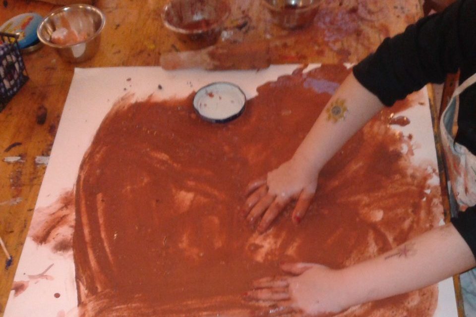 Ein Vorschulkind hat seine beide Hände volle rote Malerde auf einen weisse Blatt
